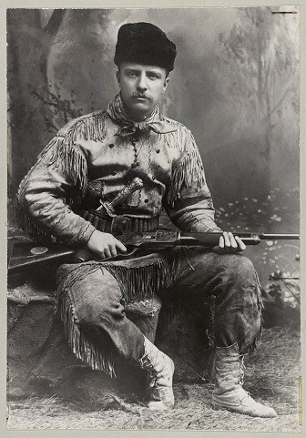 Man wearing buckskin leather clothing posed with a rifle in his lap.