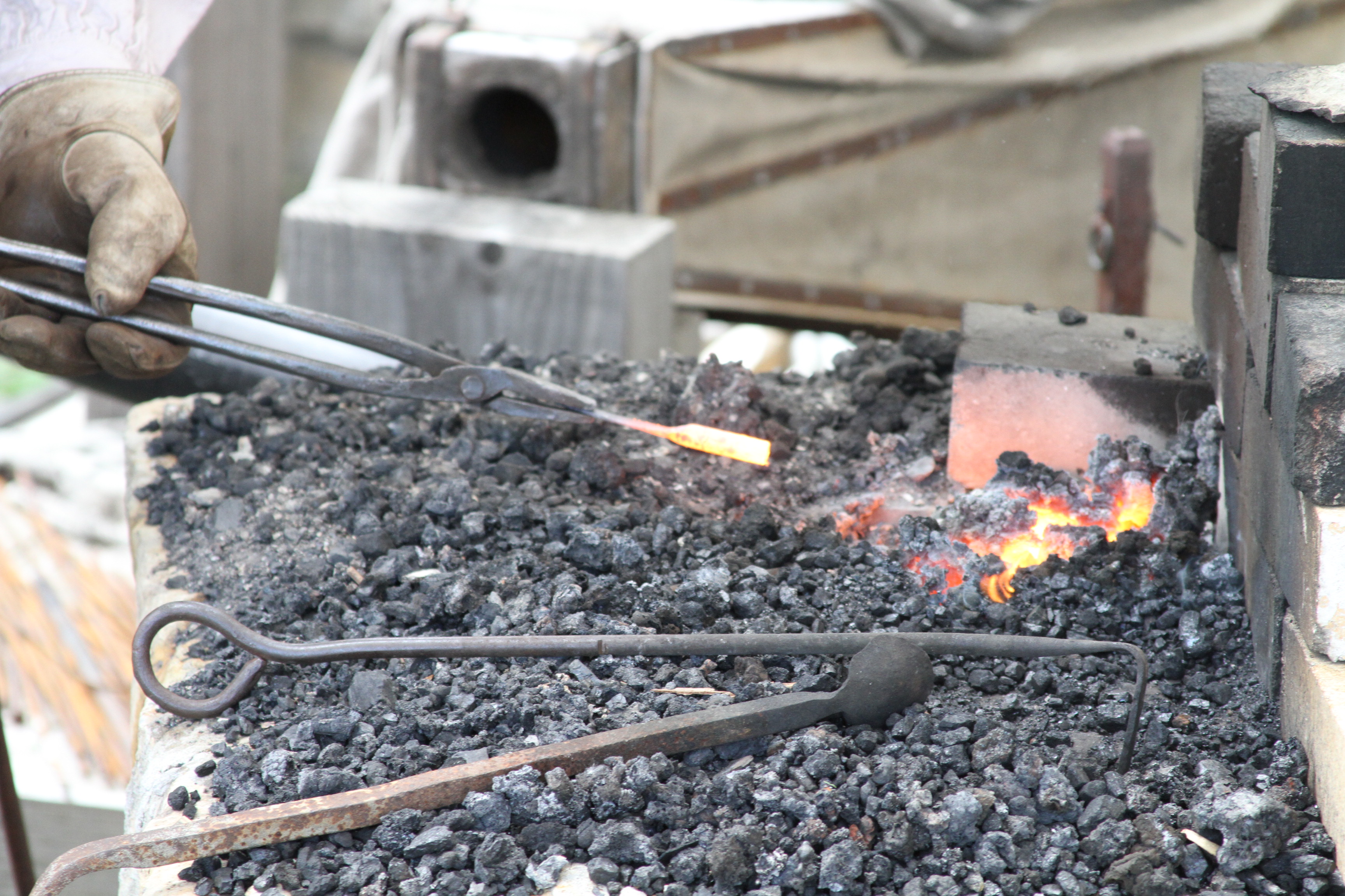 Red hot coals on blacksmith forge, a gloved hand holds tong with hot metal.