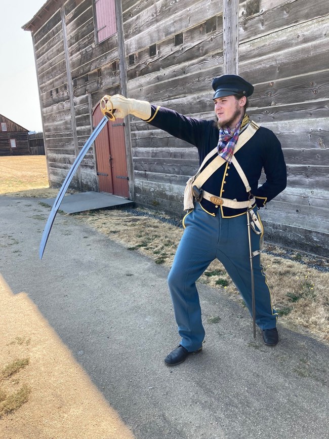 A man wearing a blue US Army Dragoons uniform holding a saber inside the reconstructed Fort Vancouver.