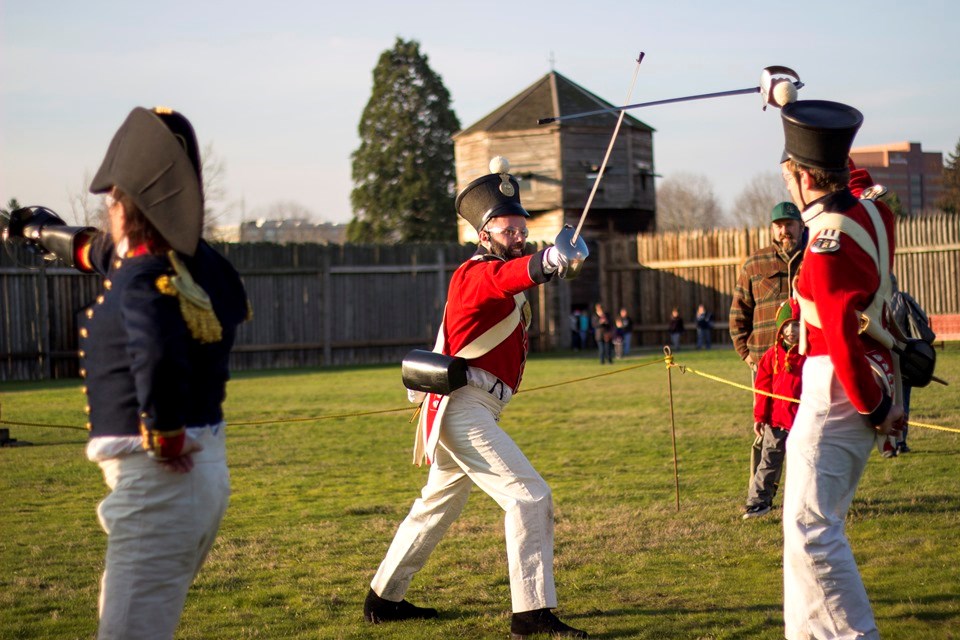 Photo of two reenactors in historic military costume inside the fort demonstrating saber techniques.