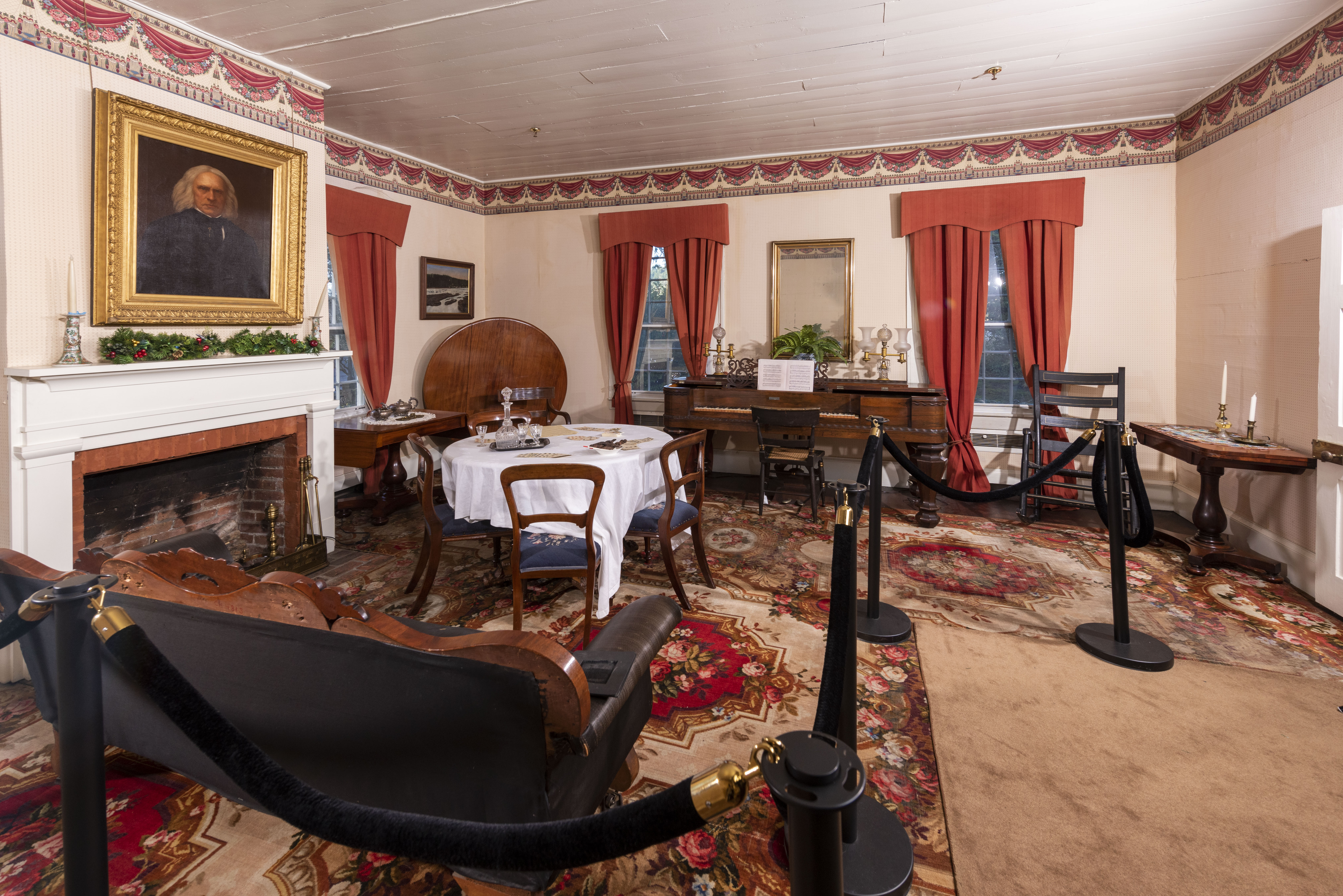 The parlor of the McLoughlin House, an ornate room with a sofa, piano, card table, and fireplace with a portrait of Dr. John McLoughlin hung over it.