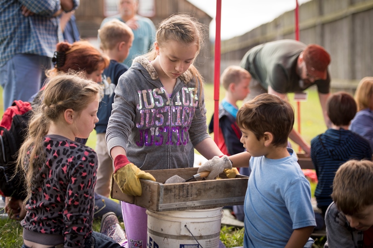 Photo of three children working together to sift dirt through a screen.