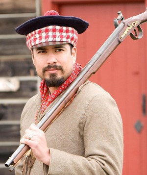 Photo of Park Ranger Aaron Ochoa in costume with a trade musket on his shoulder, portraying an employee at Fort Vancouver in the 1840s.