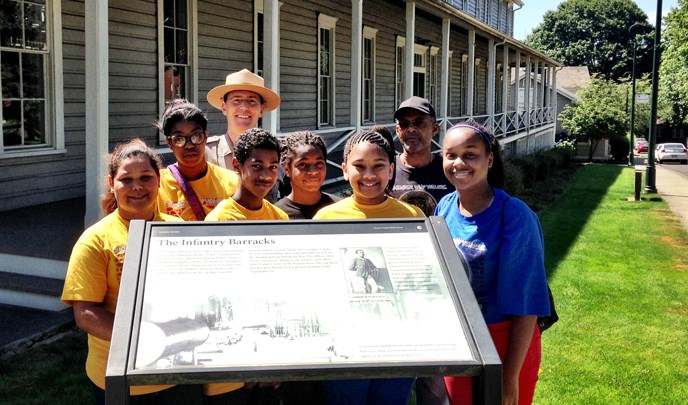 Image of park ranger and participants in NAACP Rites of Passage Academy posing beside a wayside exhibit and historic building.