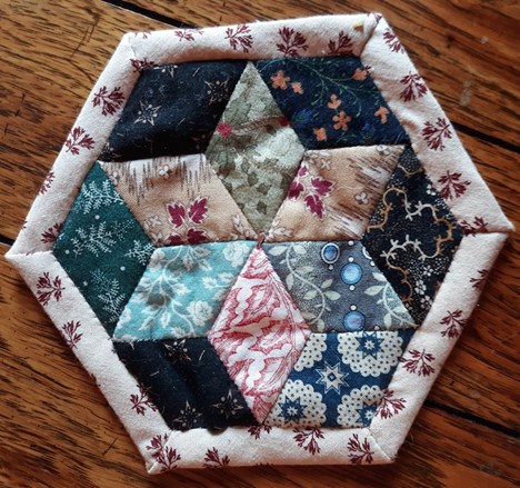 A small hexagon-shaped quilt piece made with different colors and patterns of fabric.
