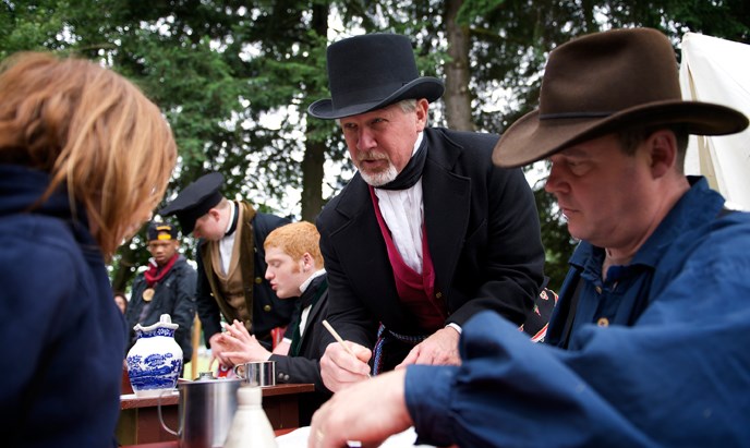 Photo of an adult aide answering a visitor question at a park event Photo of an adult aide answering a visitor question at a park event