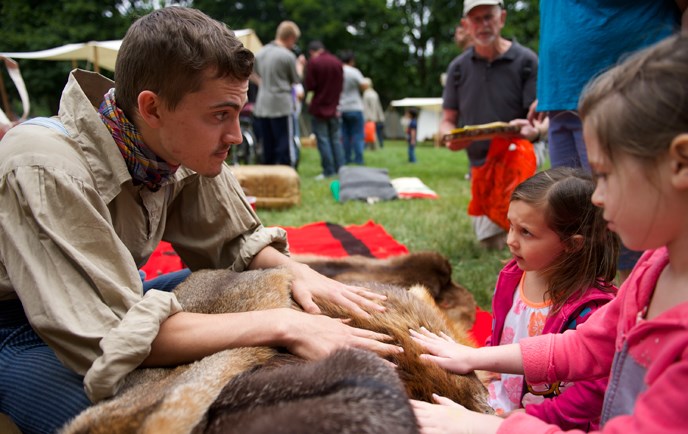 A young engage class member introduces young visitors to furs at an outdoor park event.