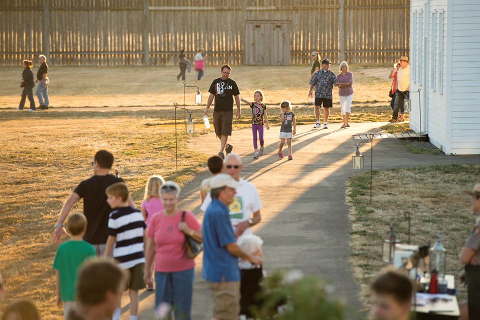 Inside Fort Vancouver at twilight, groups of people walk along paths