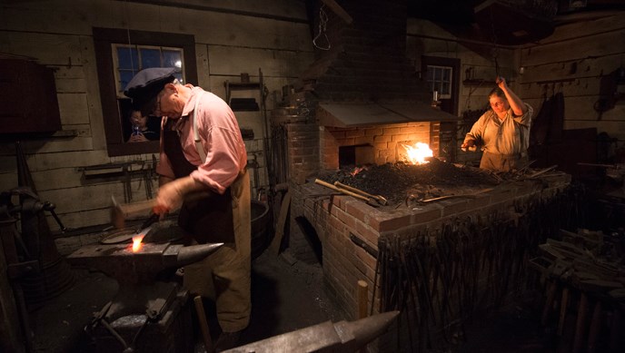 Blacksmiths working at a forge and anvil during a nighttime event at Fort Vancouver.