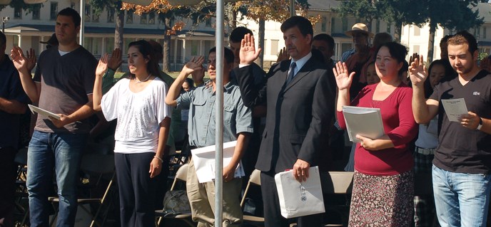 New candidates for citizenship raising their right hands under an awning, being sworn in at Fort Vancouver's Parade Ground.