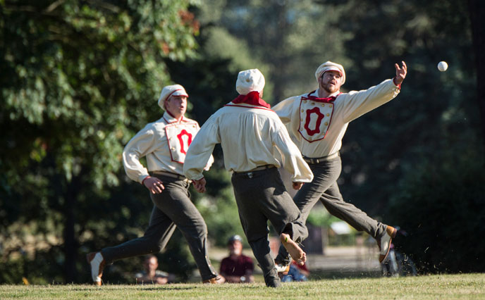 Costumed baseball players lunge for a bounding baseball.