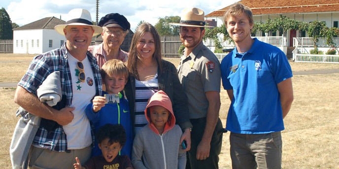 A family shows its new 4th grade park pass while posing with NPS staff in uniform and costume.