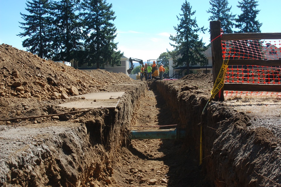 Photo of large trench through Vancouver Barracks with maintenance workers and equipment.