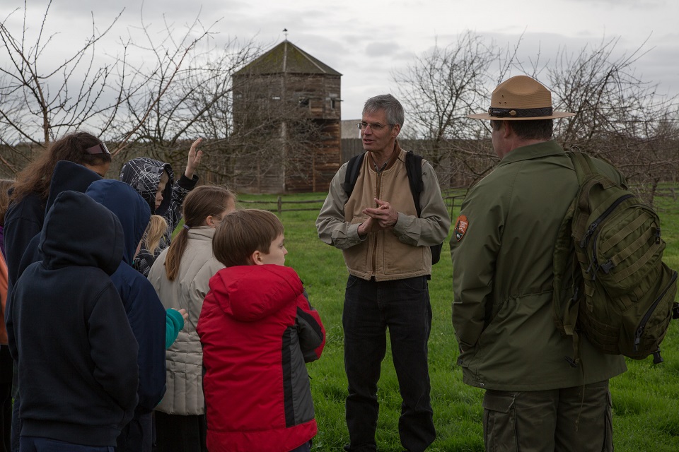 Photo of man standing near Fort Vancouver with park ranger and group of children.