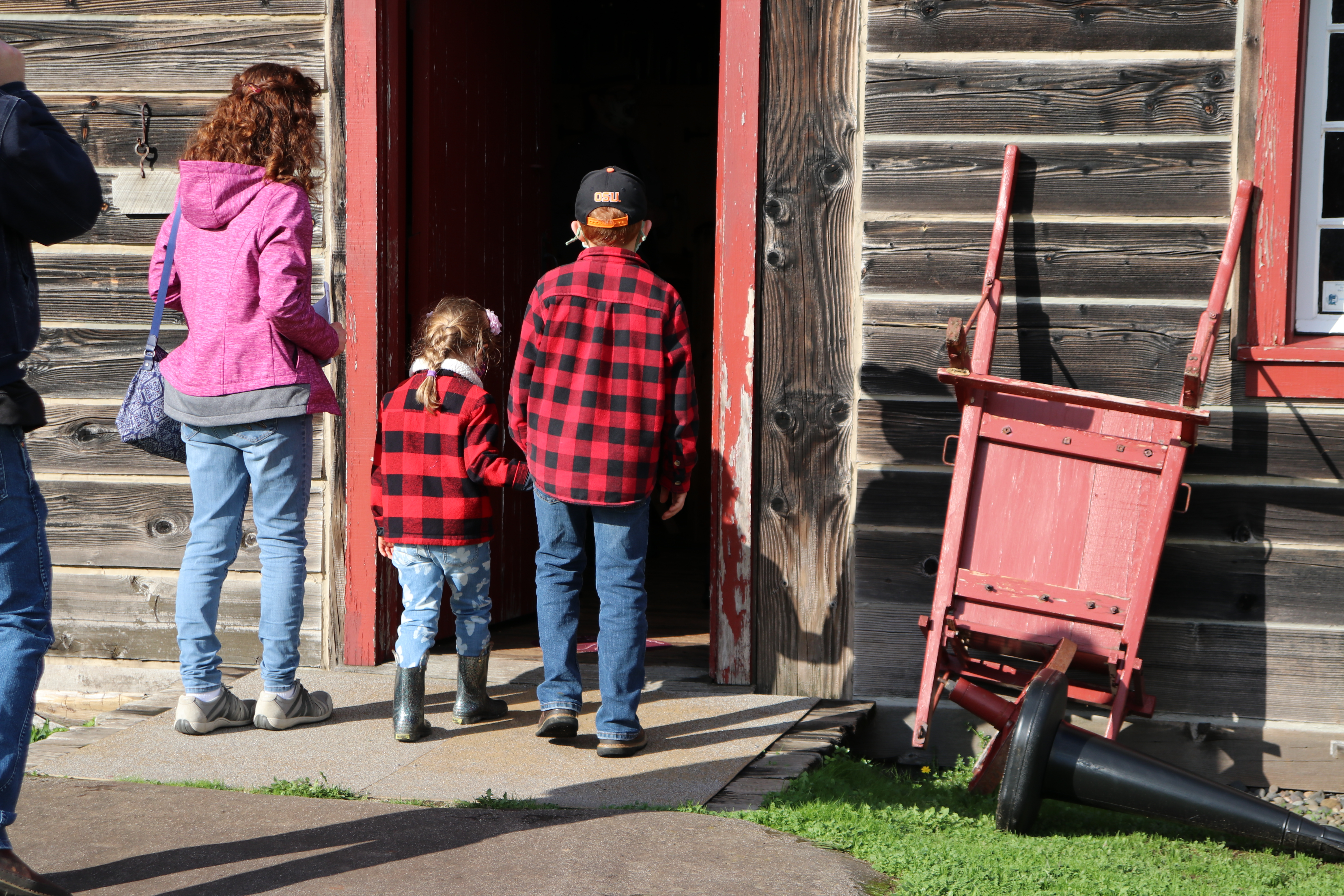 Children in red and black clothes enter wooden carpenter shop building