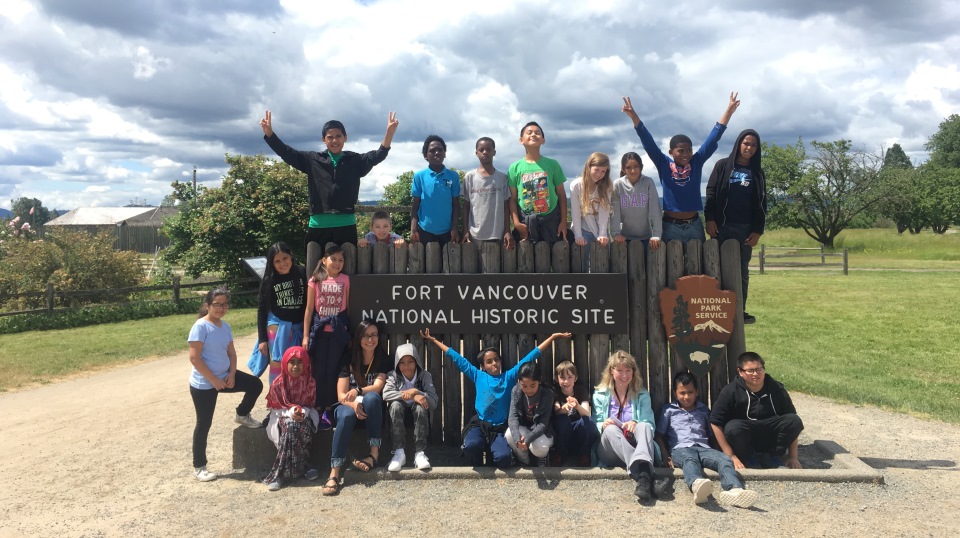 Students and teachers sit and stand around the entrance sign at Fort Vancouver