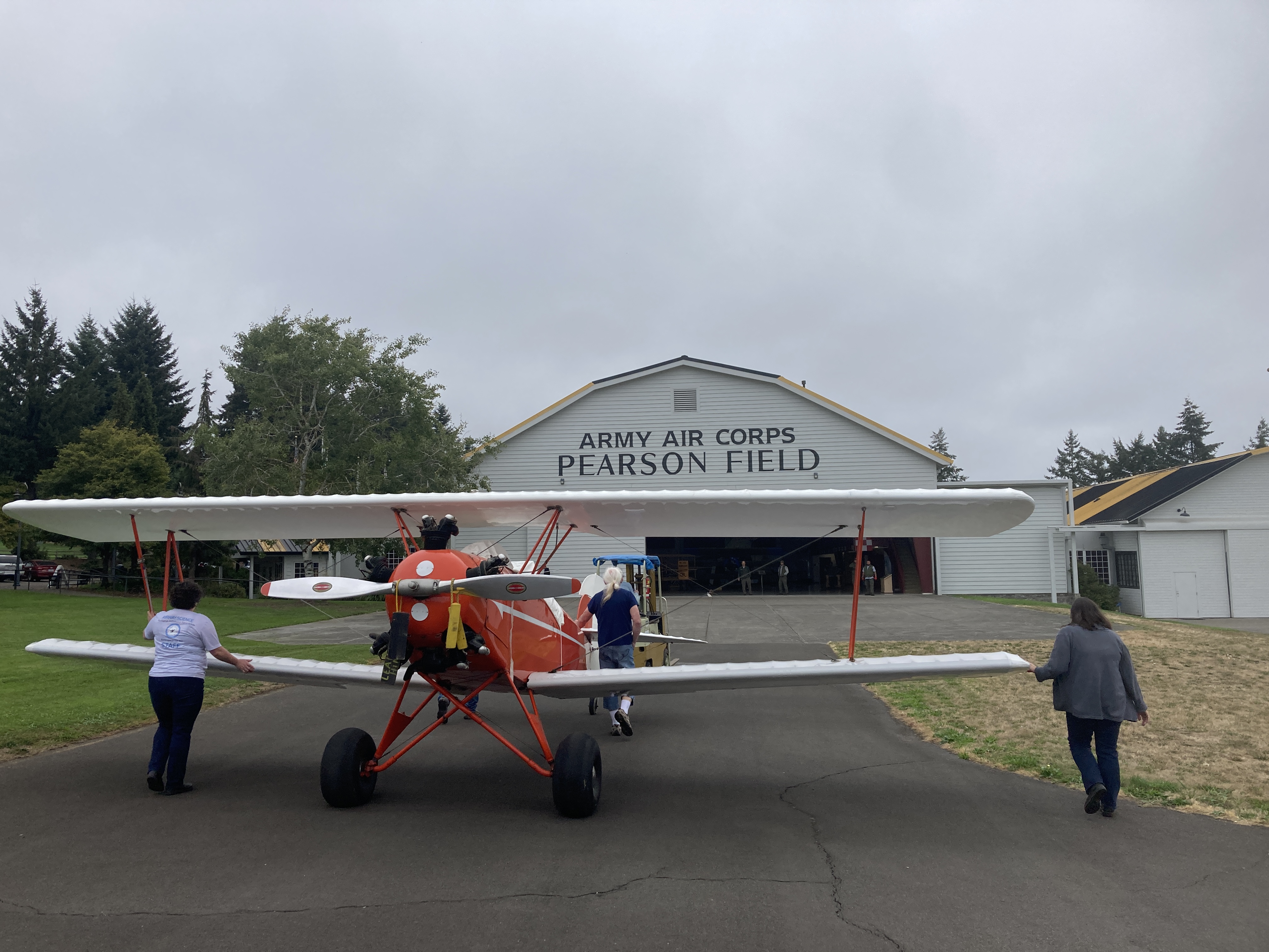 People push an orange and white aircraft into the main hangar at Pearson Air Museum.