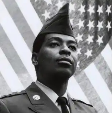Perry Watkins - US Army image Black and white photo of a Black man wearing an Army uniform standing in front of an American flag.