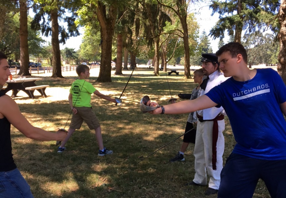 Young people hold sabers in position in mock duel