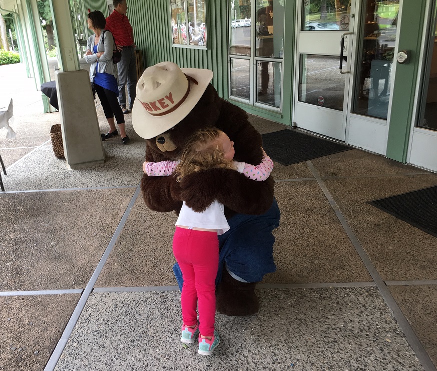 Photo of a young girl hugging the Smokey Bear mascot at the Fort Vancouver Visitor Center.