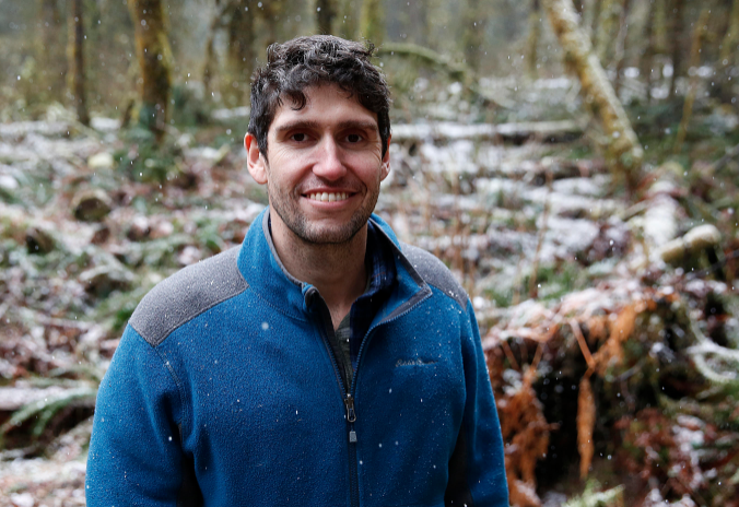 ben goldfarb Photo of a man wearing a blue sweater standing in a forest.
