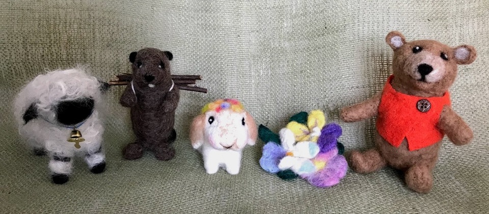 Photo of five felted items: a sheep, beaver, bunny, pansy broach, and bear.