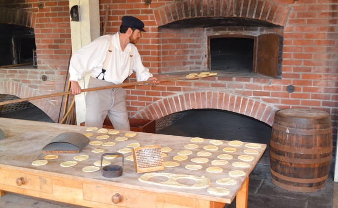 Costumed baker loads sea biscuit into the oven at the fort's Bake House Costumed baker loads sea biscuit into the oven at the fort's Bake House