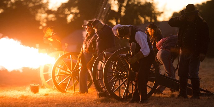 Photo of mountain howitzer firing and a large flame portruding from the howitzer's mouth.