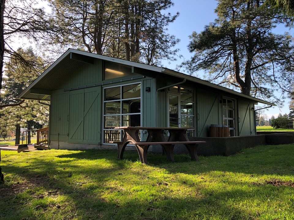 A green building with large windows and picnic benches.