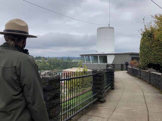 Park Ranger in foreground walks down a paved path above the Willamette River.