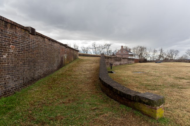 A wide grassy ramp with a brick wall on the far side leads up to the second story of a brick building in the distance.