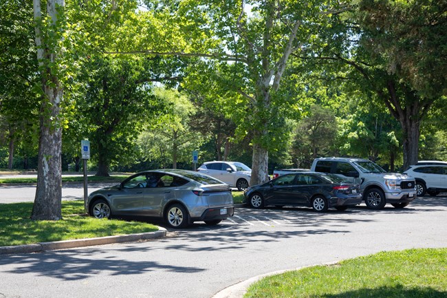 A row of parked cars in a parking lot with two marked accessible parking spaces with an access aisle between them on the end of the row.