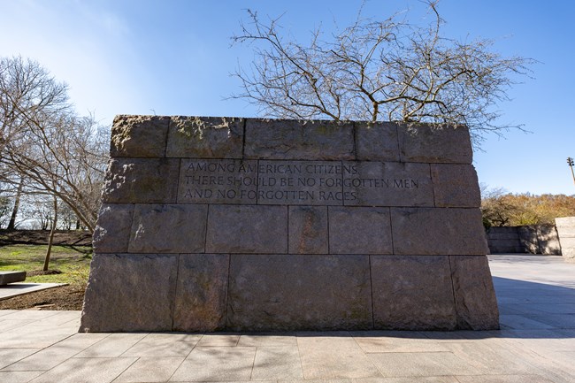 A tall, stone wall reads, "Among American citizens, there should be no forgotten men, and no forgotten races.