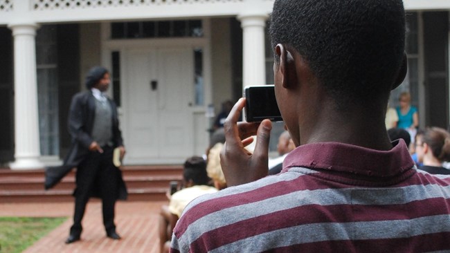 Douglass Actor performs in background while audience watches