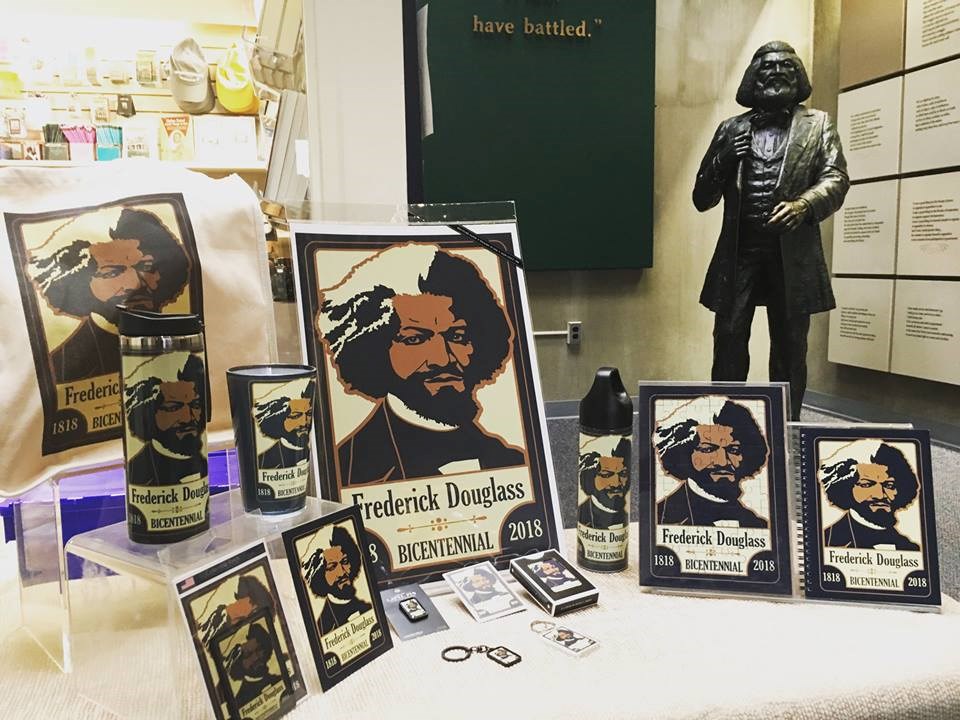 A table with posters, puzzles, coffee mugs, and other items featuring a logo with Frederick Douglass on it