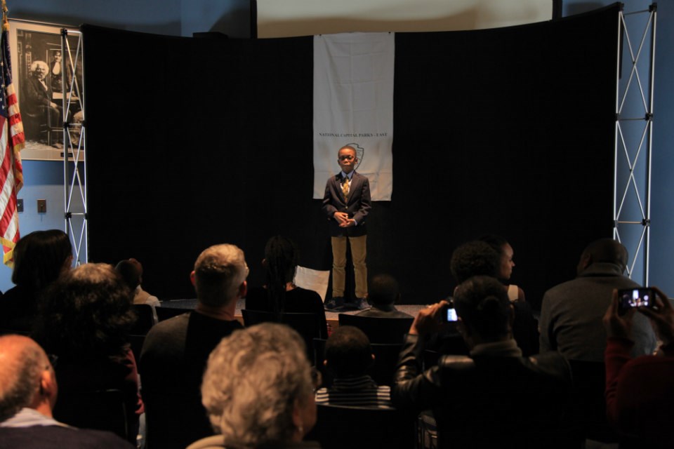 A young student speaks from a stage to a seated crowd