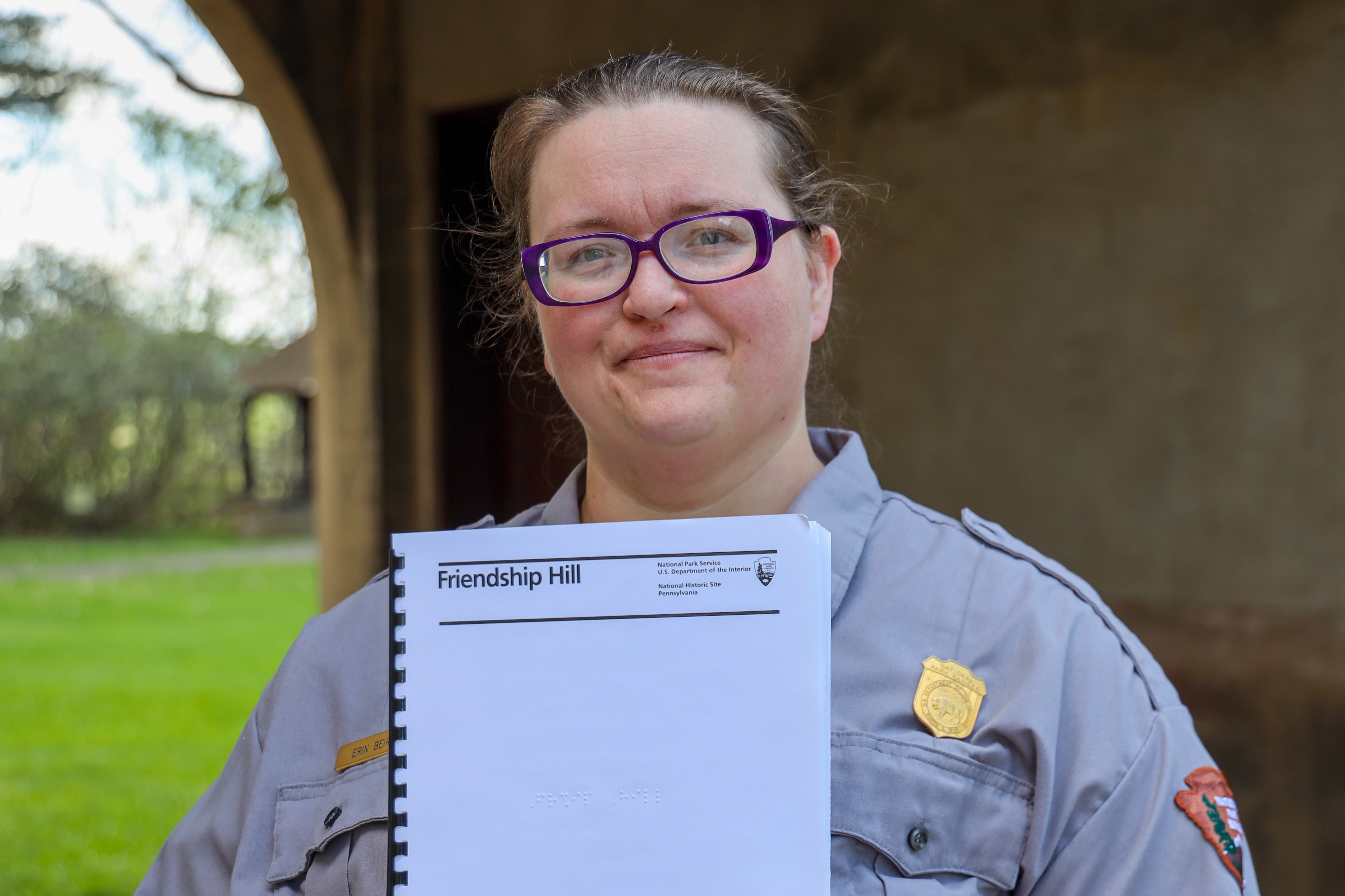 Park ranger holding up the braille park brochure at Friendship Hill
