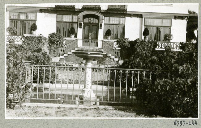 Black and white photograph of house, which is perfectly symmetrical, with plantings all throughout the area.