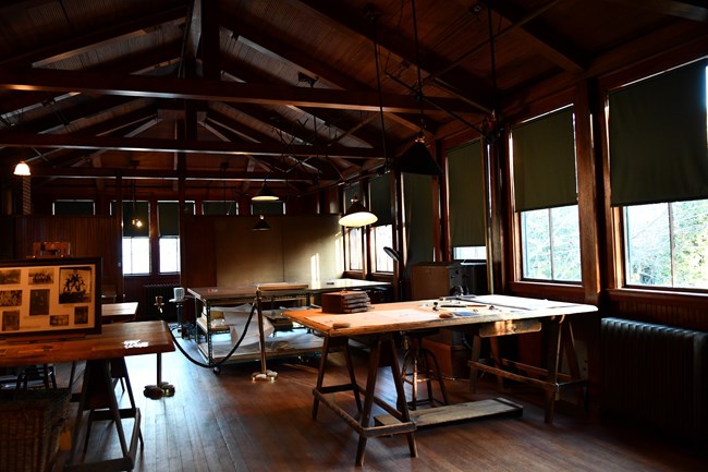 A room with many large historic drafting tables and stools