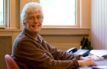 Woman sits at desk smiling.