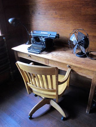 Lamp, typewriter, and fan on wooden desk and wooden chair