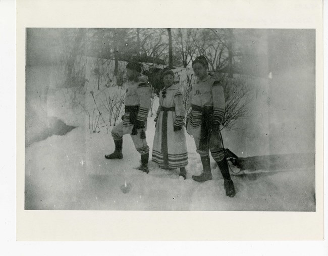 Three people in snow suits stand in snow