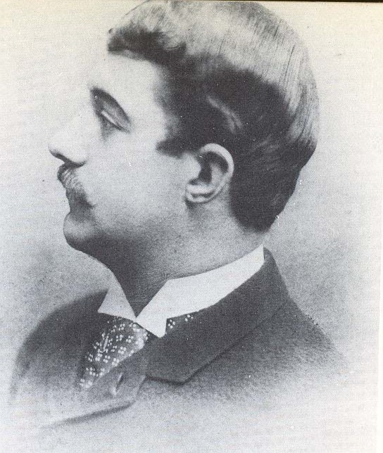Black and white of man in suit with thick dark hair looking away from camera.