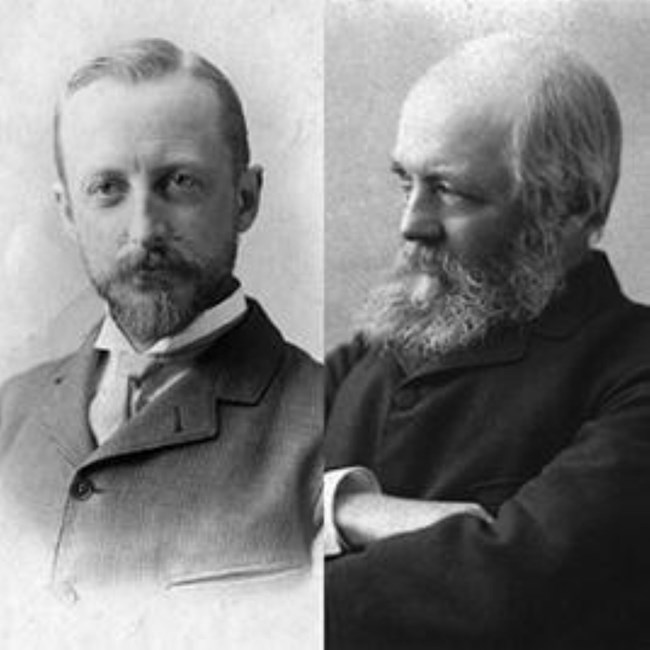 Black and white of two men posing for images in suits.