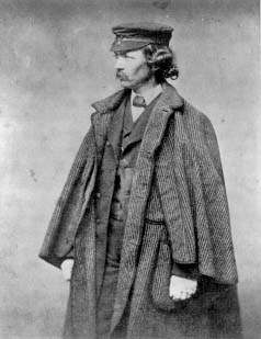 Black and white of man in jacket suit and hat posing for picture, looking away from camera.