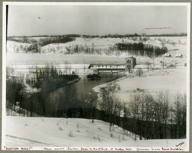 Black and white river running through snow covered hills with lots of open space, and very few trees still with leaves.