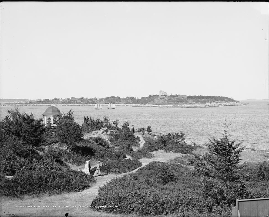 Black and white of rocky and sandy area near ocean with some people walking around