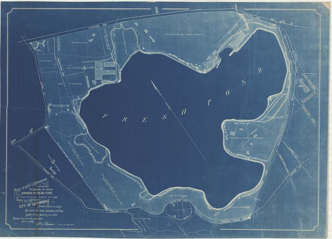 Blue paper with white lines showing a pond with small roads near it, and larger roads as a rectangular boarder.