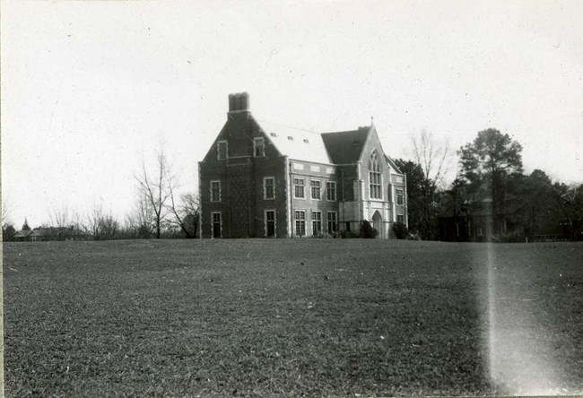 Grassy area with large building on it and some trees behind it