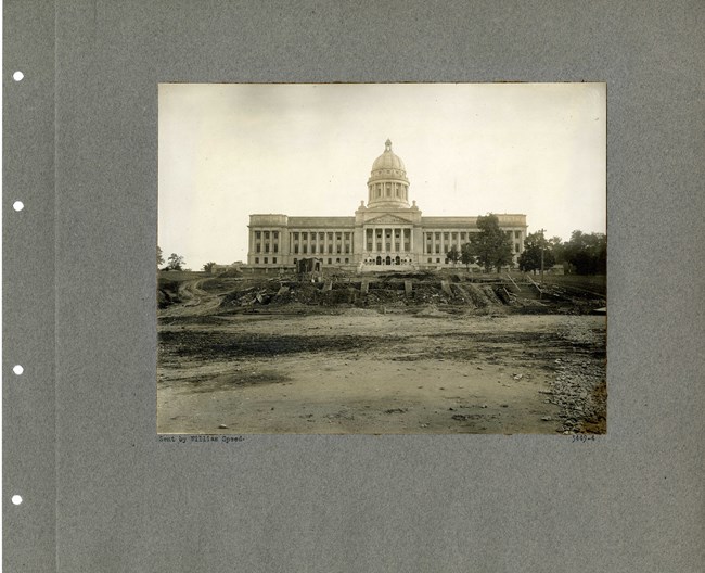 Black and white photograph of large white building looking like white house perched on a hill